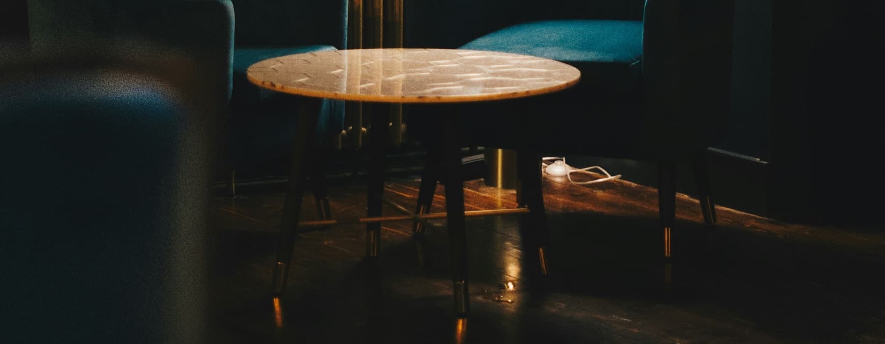 An empty round table between two armchairs in a dark bar, lit by a single lamp